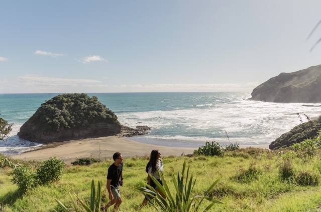 Young couple exploring the coastal cliffs at O'Neill Bay as they hike the Te Henga Walkway on a sunny day